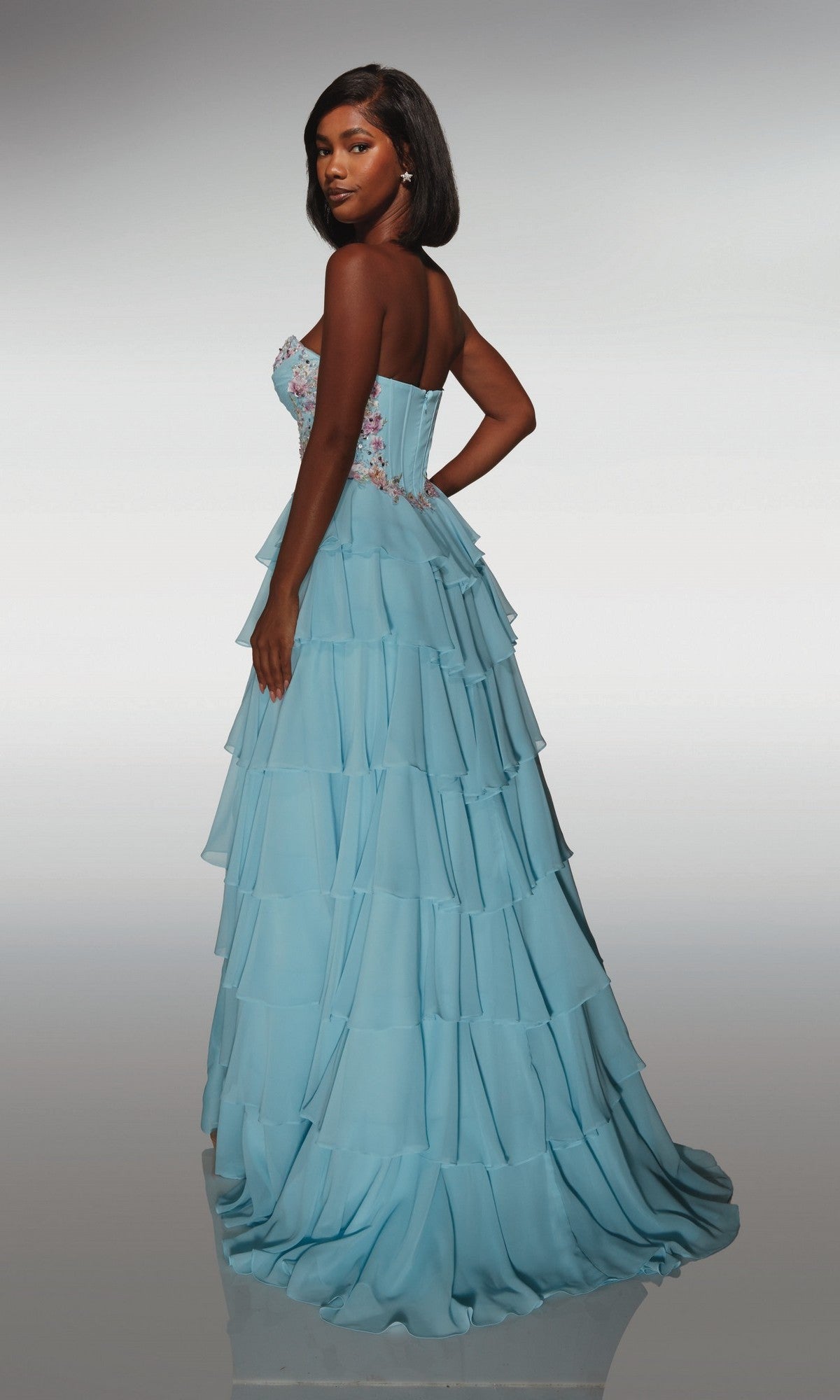 A woman poses with her back slightly turned, showcasing the Alyce 62013 long prom dress—strapless chiffon with a corset bodice and delicate floral embroidery.